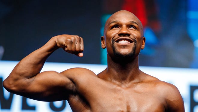 Floyd Mayweather flexes as he stands on the scales during weigh-ins for his upcoming boxing match at T-Mobile Arena.