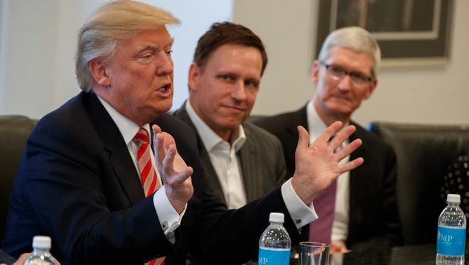 Apple CEO Tim Cook, right, and PayPal founder Peter Thiel, center, listen as President-elect Donald Trump speaks during a meeting with technology industry leaders at Trump Tower in New York, Wednesday, Dec. 14, 2016. Cook is among tech CEOs urging Trump to keep the U.S. in the Paris climate accord.