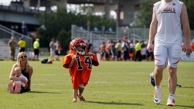 Cincinnati Bengals quarterback Andy Dalton walks off the practice field as his son wears his equipment.