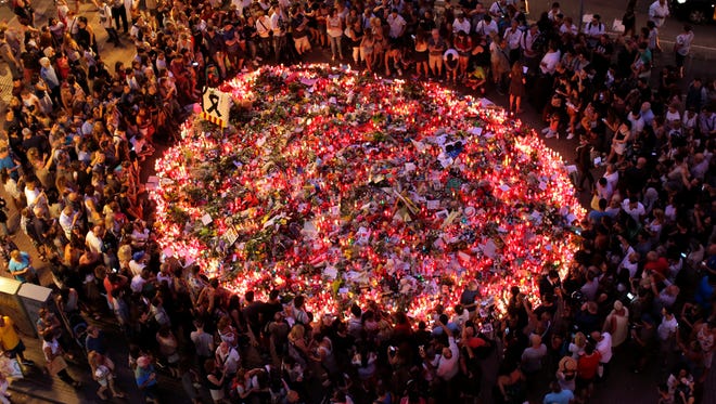 People pay respect at a memorial tribute of flowers, messages and candles to the victims on Barcelona's historic Las Ramblas promenade on the Joan Miro mosaic, embedded in the pavement where the van stopped after killing at least 13 people in Barcelona, Spain on Aug. 19, 2017.