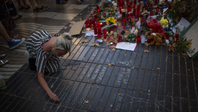 A woman writes a message on the ground as a memorial tribute after the recent attack that left many killed and wounded in Barcelona, Spain on Aug. 24, 2017.