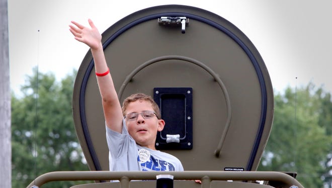 Riley Borchardt, 12, of Fredonia waves to family members from the top port of a tactical vehicle parked at a  FBI display during Saukville's National Night Out at Grady Park on Aug. 15.