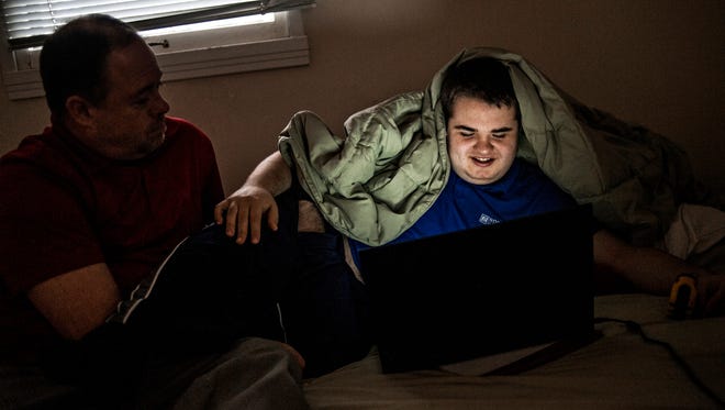 In a Dec. 16, 2015 photo, Dennis Mashue watches his son Tucker Mashue, 17, work on a cyber school lesson at their home in Midland, Mich. (Erin Kirkland/Midland Daily News via AP)