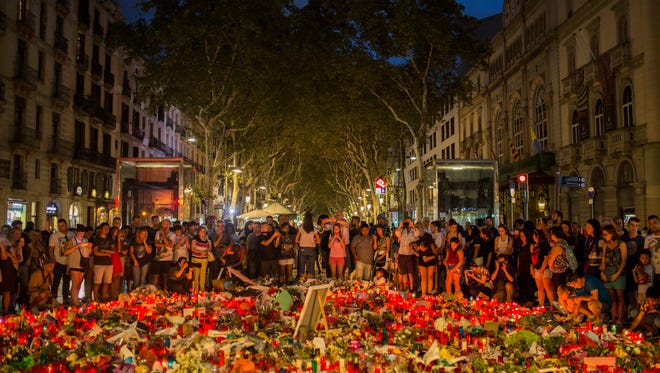People stand next to candles and flowers placed on the ground, after a terror attack that left many killed and wounded in Barcelona, Spain on Aug. 20, 2017.
