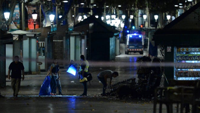 Policemen check the area after towing away the van which plowed into the crowd, killing at least 13 people and injuring around 100 others on the Rambla in Barcelona on Aug. 18, 2017.