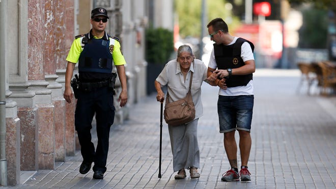Policemen accompany an elderly woman near a cordoned off area.