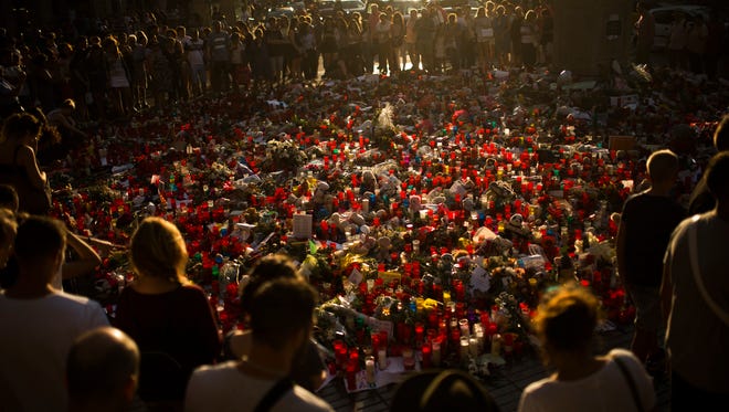 People stand next to candles and flowers placed on the ground for the victims of an attack that left many killed and wounded in Barcelona, Spain on Aug. 24, 2017.