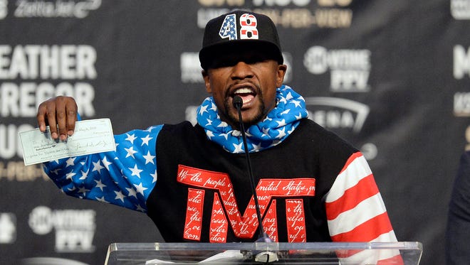 Floyd Mayweather holds up a check while speaking during a world tour press conference to promote the upcoming Mayweather vs McGregor boxing match.