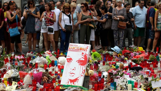 People stand next to candles and flower tributes placed on the ground after a terror attack that killed 14 people and wounded over 120 in Barcelona, Spain on Aug. 20, 2017. Police put up scores of roadblocks across northeast Spain on Sunday in hopes of capturing a fugitive suspect at large following the vehicle attack.