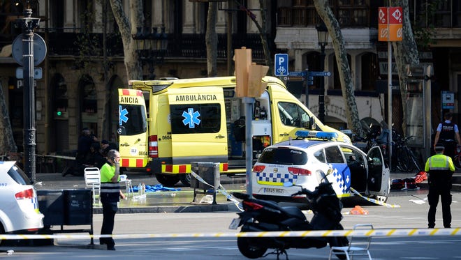 A policemen and a medical staff member stand near police cars and an ambulance in a cordoned off area after a van ploughed into a crowd, injuring several persons on the Rambla in Barcelona on Aug. 17, 2017.