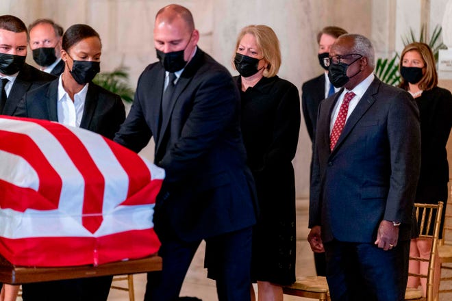 US Supreme Court Justice Clarence Thomas (R) and his wife Virginia Thomas, (C) watch as the flag-draped casket of Justice Ruth Bader Ginsburg arrives at the Supreme Court in Washington, DC, on Sept. 23, 2020.